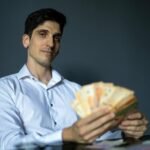 Businessman in a white shirt holding Argentine pesos with a confident expression indoors.
