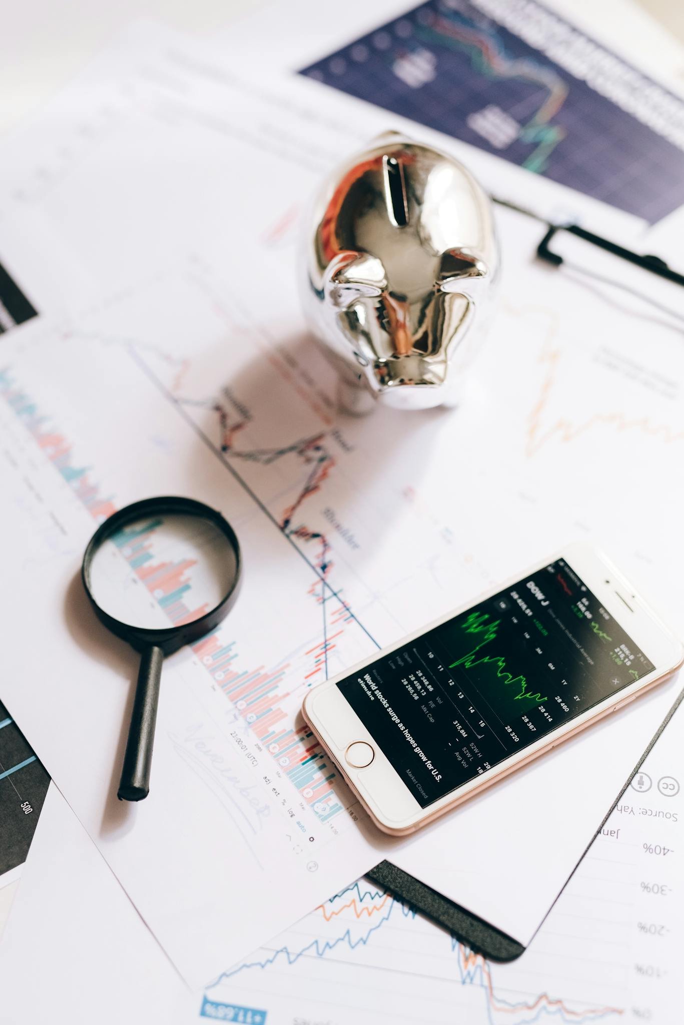 Smartphone displaying stock market, piggy bank, and magnifying glass on financial charts.